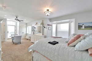 Carpeted bedroom featuring a textured ceiling, vaulted ceiling, and ceiling fan