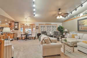 Carpeted living room with ceiling fan with notable chandelier, vaulted ceiling, and rail lighting