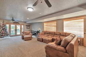 Carpeted living room with a textured ceiling, ceiling fan, and french doors