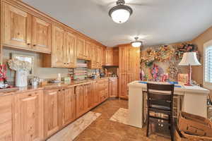 stone counters, light brown cabinets, a breakfast bar, and a healthy amount of sunlight