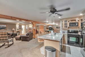 Basement Kitchen with kitchen peninsula, black appliances, a kitchen bar, ceiling fan, and light carpet