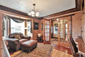 Living room featuring a textured ceiling, light hardwood / wood-style floors, ornamental molding, and french doors