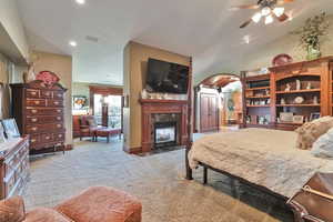 Carpeted bedroom featuring vaulted ceiling, ceiling fan, a fireplace, and a textured ceiling