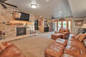 Carpeted living room with a textured ceiling, a stone fireplace, ceiling fan, and french doors