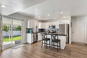 Kitchen with stainless steel appliances, white cabinetry, wood-type flooring, and a kitchen bar