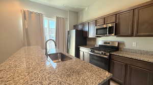 Kitchen featuring light stone countertops, a kitchen island with sink, sink, and stainless steel appliances