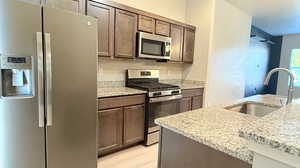 Kitchen with light hardwood / wood-style flooring, stainless steel appliances, light stone countertops, and sink