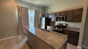 Kitchen with light hardwood / wood-style floors, stainless steel appliances, dark brown cabinets, a center island with sink, and sink