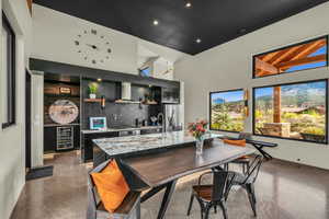 Kitchen featuring a kitchen island with sink, stainless steel appliances, tasteful backsplash, wine cooler, and wall chimney exhaust hood