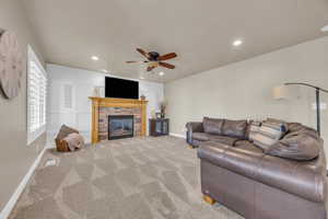 Carpeted living room with ceiling fan and a stone fireplace