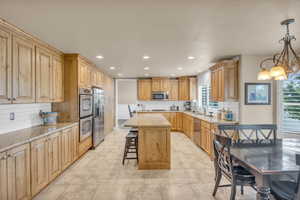 Kitchen with a chandelier, a center island, decorative backsplash, appliances with stainless steel finishes, and decorative light fixtures