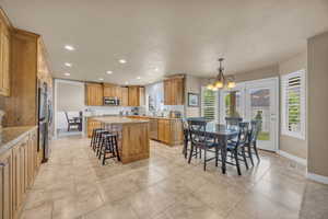 Kitchen with a notable chandelier, a kitchen island, backsplash, appliances with stainless steel finishes, and light stone countertops