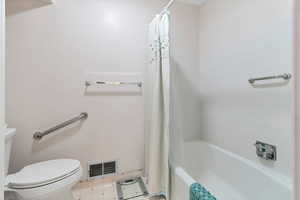 Bathroom featuring shower / tub combo with curtain, tile patterned flooring, and toilet