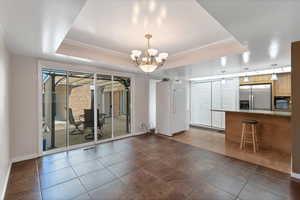 Interior space featuring dark tile patterned flooring, a chandelier, a raised ceiling, and crown molding