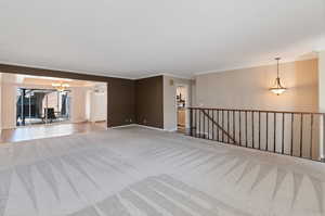 Spare room with ornamental molding, an inviting chandelier, and light colored carpet