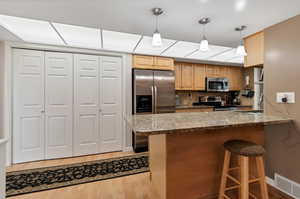 Kitchen featuring light stone counters, decorative light fixtures, backsplash, appliances with stainless steel finishes, and light wood-type flooring