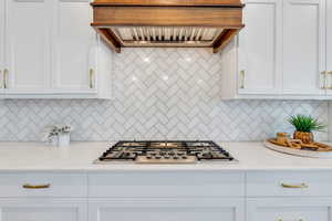 Kitchen with light stone counters, stainless steel gas cooktop, custom range hood, and white cabinetry