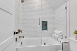 Bathroom with lofted ceiling, a textured ceiling, shower / bath combination with glass door, and toilet