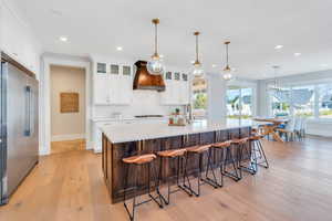 Kitchen with light hardwood / wood-style floors, premium range hood, a large island with sink, and stainless steel appliances