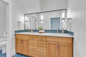 Bathroom featuring double vanity, lofted ceiling, toilet, tasteful backsplash, and tile patterned flooring