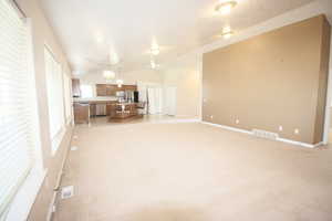 Unfurnished living room with a textured ceiling, vaulted ceiling, a chandelier, and light colored carpet