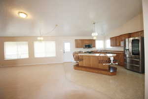 Kitchen featuring a healthy amount of sunlight, pendant lighting, lofted ceiling, appliances with stainless steel finishes, and a center island