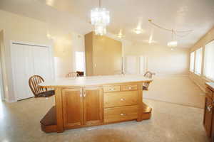 Kitchen featuring light colored carpet, decorative light fixtures, a center island, and vaulted ceiling