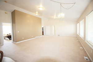 Carpeted spare room featuring lofted ceiling, plenty of natural light, a notable chandelier, and a textured ceiling