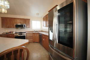 Kitchen featuring lofted ceiling, hanging light fixtures, sink, stainless steel appliances, and an inviting chandelier