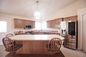 Kitchen featuring light carpet, decorative light fixtures, vaulted ceiling, a notable chandelier, and stainless steel appliances