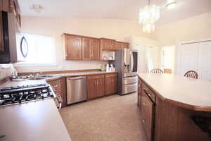 Kitchen featuring hanging light fixtures, a breakfast bar area, appliances with stainless steel finishes, an inviting chandelier, and vaulted ceiling