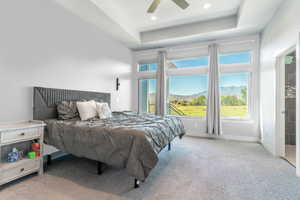 Bedroom featuring a raised ceiling, a mountain view, ceiling fan, and light colored carpet