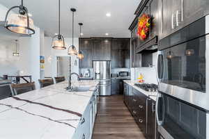 Kitchen with pendant lighting, a kitchen island with sink, dark hardwood / wood-style floors, light stone countertops, and stainless steel appliances