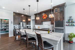 Kitchen with pendant lighting, light marble counters, dark flooring, a large island with sink, and appliances with stainless steel finishes