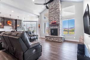 Living room featuring ceiling fan with notable chandelier, a stone fireplace, dark hardwood / wood-style flooring, and high vaulted ceiling