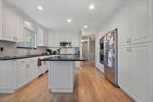 Kitchen with appliances with stainless steel finishes, light hardwood / wood-style floors, white cabinets, a center island, and sink