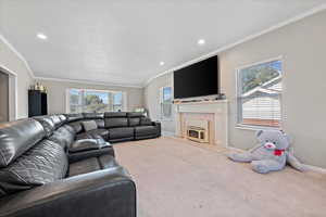 Carpeted living room featuring vaulted ceiling, a premium fireplace, and crown molding