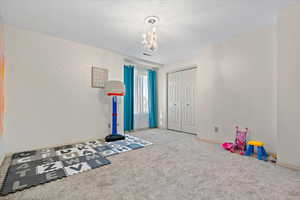 Recreation room featuring carpet floors, a textured ceiling, and a notable chandelier