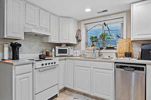 Kitchen featuring white stove, sink, ventilation hood, white cabinets, and stainless steel dishwasher