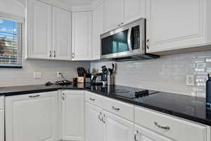 Kitchen with black electric cooktop, tasteful backsplash, and white cabinetry