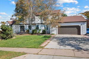 View of property hidden behind natural elements featuring a garage and a front lawn