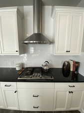 Kitchen featuring decorative backsplash, white cabinets, wall chimney range hood, and stainless steel gas cooktop