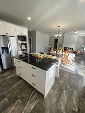 Kitchen featuring pendant lighting, white cabinets, a notable chandelier, a kitchen island, and stainless steel appliances