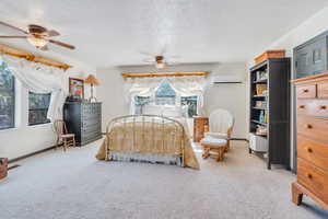 Carpeted bedroom featuring ceiling fan, a textured ceiling, multiple windows, and an AC wall unit