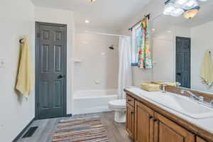 Full bathroom featuring wood-type flooring, vanity, toilet, and shower / bathtub combination with curtain