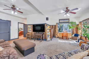 Carpeted living room with wooden walls, ceiling fan, and a wealth of natural light