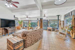 Living room with a healthy amount of sunlight, light tile patterned floors, ceiling fan, and a wood stove