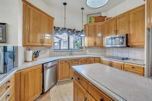 Kitchen featuring backsplash, appliances with stainless steel finishes, hanging light fixtures, and sink