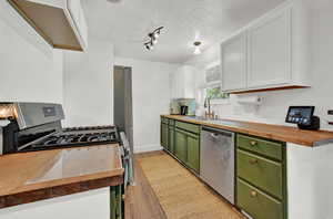 Kitchen with white cabinetry, butcher block countertops, dishwasher, green cabinetry, and sink