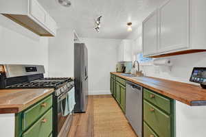 Kitchen with sink, butcher block countertops, green cabinetry, white cabinetry, and appliances with stainless steel finishes